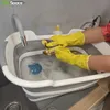 A person wearing yellow gloves is washing dishes in a collapsible sink. Voir les images du produit