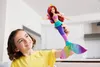 A young girl is holding up a mermaid doll. Anteprima dell’immagine prodotto
