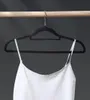 A white camisole hangs from a black velvet hanger on a wooden rod. Anteprima dell’immagine prodotto