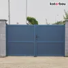 A blue metal gate with a handle, set between two concrete pillars, in front of a gravel driveway. Náhled obrázku produktu