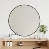 A round black-rimmed mirror is mounted on a white wall above a wooden vanity with various cosmetic products. Voir les images du produit