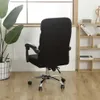 A black office chair cover is shown from the back, placed on a black office chair. The chair has a chrome base with wheels. In the background, there is a window with blinds, a plant in a white basket, and a wooden shelf unit with books and decorative items Voir les images du produit