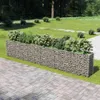 A gabion planter filled with plants sits on a paved patio next to a grassy lawn and trees. Náhled obrázku produktu
