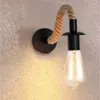 A single wall lamp with a rope arm and a clear Edison bulb is mounted on a textured wall. Náhľad obrázku produktu