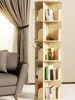A rotating bookshelf filled with books and decorative items is placed next to a sofa and a curtained window. Produktbild-Vorschau