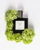 A perfume bottle surrounded by green flowers on a white background. Podgląd zdjęcia produktu