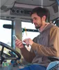 A man is sitting in a tractor cab, looking at his smartphone. Produktbild-Vorschau