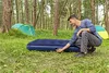 A man is kneeling and adjusting an air mattress in a campsite setting, with a tent in the background. Anteprima dell’immagine prodotto