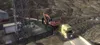 A truck carrying an excavator on a trailer drives on a winding road in a mountainous area. Produktbild-Vorschau