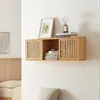 A wooden wall shelf with two slatted doors is mounted on a white wall above a bed. Produktbild-Vorschau