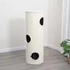 A tall, cylindrical cat scratching post with multiple circular openings is shown in a room with light gray flooring and white walls. Produktbild-Vorschau