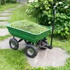A green garden cart filled with grass clippings is parked on a concrete path next to a lush green bush with white flowers. Produktbild-Vorschau