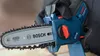 A close-up shot of a person holding a small blue Bosch chainsaw. Náhľad obrázku produktu