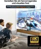 Two people are playing a video game on a large TV, with a docking station visible on the TV stand. The image includes marketing text and graphics. Produktbild-Vorschau