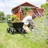 A person is gardening in a backyard with a wooden shed and a garden cart filled with flowers. Náhled obrázku produktu