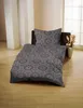 A bed with patterned bedding is set up in a room with wooden floors and white pillars. Náhled obrázku produktu