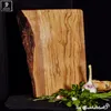 A wooden cutting board with a natural edge, displayed with fresh herbs, garlic, and bread on a dark surface. Produktbild-Vorschau