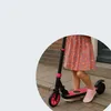 A child's legs and a pink scooter on a paved sidewalk. Anteprima dell’immagine prodotto