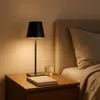 A bedside table with a lamp, book, and glass of water next to a bed. Produktbild-Vorschau