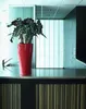 A red planter with a plant on a counter in a modern kitchen or office setting. Náhled obrázku produktu