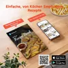 A recipe book and a smartphone displaying recipes are placed on a wooden table, with a plate of french fries in the background. Produktbild-Vorschau