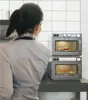 A person is looking at two stacked microwaves in a kitchen setting. Náhľad obrázku produktu