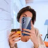 A woman takes a selfie while holding a coffee cup and a phone with a clear case. Náhľad obrázku produktu