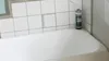 A can of spray foam sits on the edge of a bathtub next to white tiles. Produktbild-Vorschau
