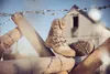 A pair of beige tactical boots are placed on a wooden barrier with barbed wire, with a building in the background. Produktbild-Vorschau