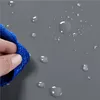 A hand holding a blue cloth wiping water droplets off a gray surface. Produktbild-Vorschau