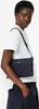 A woman wearing a white top and dark blue pants, holding a dark blue satchel bag. Produktbild-Vorschau