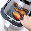 A hand is using red tongs to place sweet potatoes into a gray silicone liner inside a white air fryer. Náhľad obrázku produktu