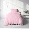 A pink duvet and pillow are neatly arranged on a bed, with a floor lamp and a nightstand with flowers in the background. Produktbild-Vorschau