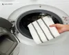A hand is holding a striped towel in front of an open washing machine. Produktbild-Vorschau