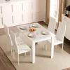 A white dining table set with four white chairs, set with plates, cutlery, and a bowl of fruit. Produktbild-Vorschau