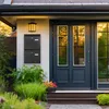 A front view of a modern house entrance with a dark blue door, flanked by windows, and a black double mailbox mounted on the wall. Produktbild-Vorschau