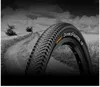 A close-up of a bicycle tire on a dirt road with fields and trees in the background. Produktbild-Vorschau