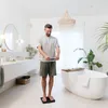 A man is using a digital scale in a modern bathroom with a bathtub and plants. Produktbild-Vorschau