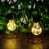 Two solar-powered diamond-shaped lanterns with warm white LED lights are placed on a wooden surface in front of a green leafy background. Produktbild-Vorschau