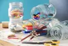 A collection of Kilner jars filled with various office supplies, arranged on a surface with a blue background. Voir les images du produit