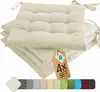 A stack of cream-colored seat cushions with ties, a product tag, and a color swatch strip. Náhled obrázku produktu