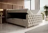 A tufted beige boxspring bed with its storage compartment open, set in a modern bedroom with wood paneling and large windows. Produktbild-Vorschau