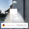 An outdoor LED light fixture with a motion sensor mounted on a textured wall, with a house and garden visible in the background. Produktbild-Vorschau