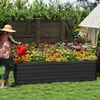 A woman watering a raised garden bed filled with colorful flowers. Voir les images du produit