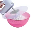 A hand is holding a white and gray electric mixer over a pink bowl filled with white powder, with a clear plastic splash guard between the mixer and the bowl. Produktbild-Vorschau