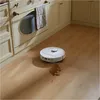 A white robot vacuum cleaner is cleaning up a spill on a light wood floor in a kitchen setting. Náhled obrázku produktu