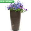 A tall, brown rain barrel filled with blue and purple flowers, set against a white background. Produktbild-Vorschau