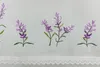 A close-up of embroidered lavender flowers on a white fabric with lace trim. Produktbild-Vorschau