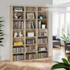 A wooden bookshelf filled with DVDs, CDs, books, and decorative items, placed in a room with a window and furniture visible in the background. Náhled obrázku produktu