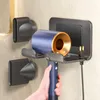A hand is holding a blue and gold hair dryer, which is mounted on a gray wall holder. The holder is attached to a tiled wall. Produktbild-Vorschau